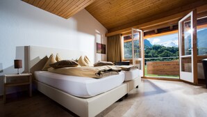 A bedroom with a large bed, wooden ceiling, and a view of a mountain through open windows. - Jungfrau Hotel (Wilderswil)