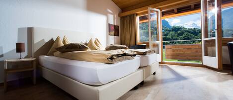 A bedroom with a large bed, wooden ceiling, and a view of a mountain through open windows.