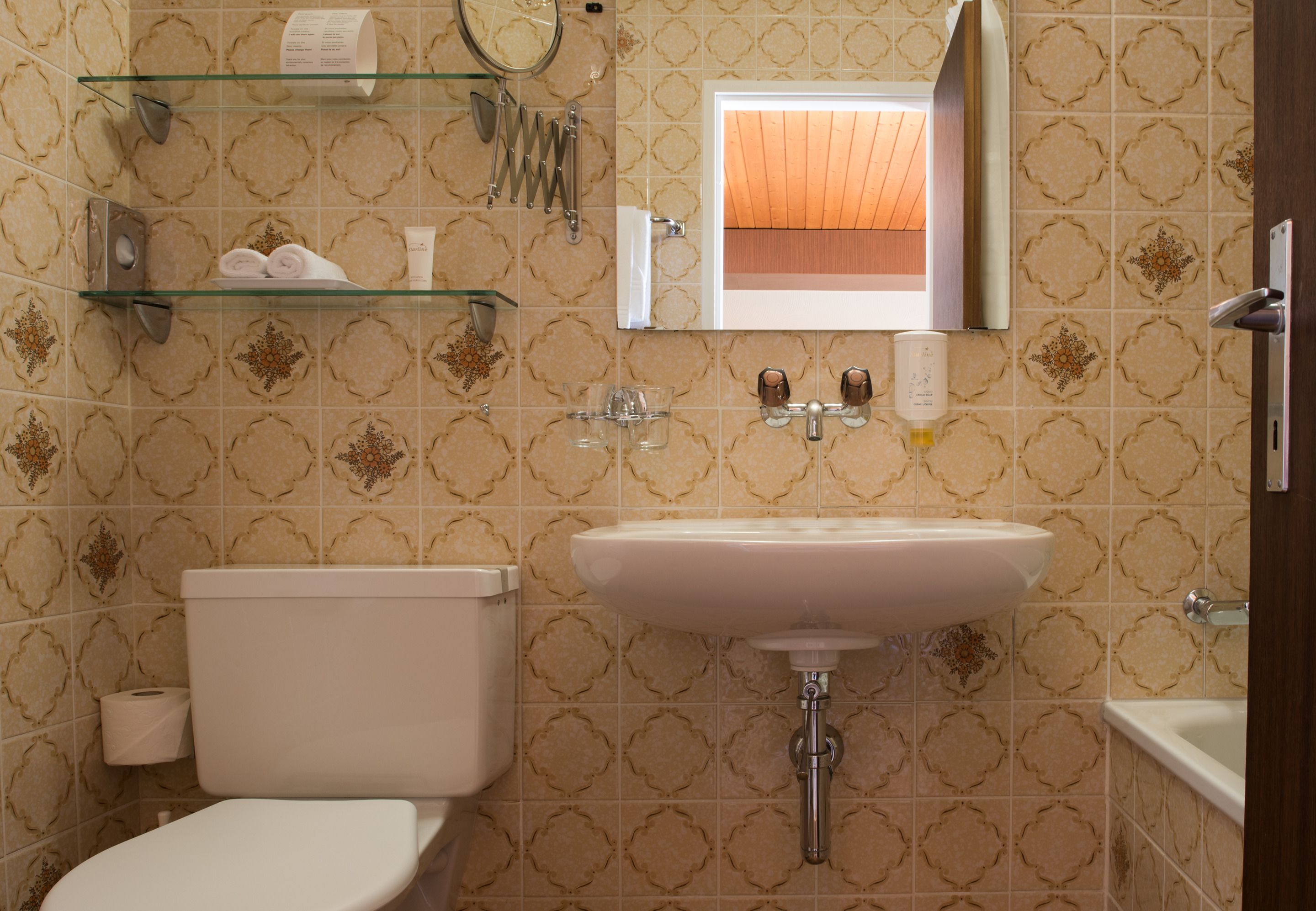 A bathroom with a toilet, sink, and glass shelves with toiletries.