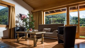 A modern living room with a wooden table, a sofa, and a chair. There is a large window with a mountain view. - Jungfrau Hotel (Wilderswil)