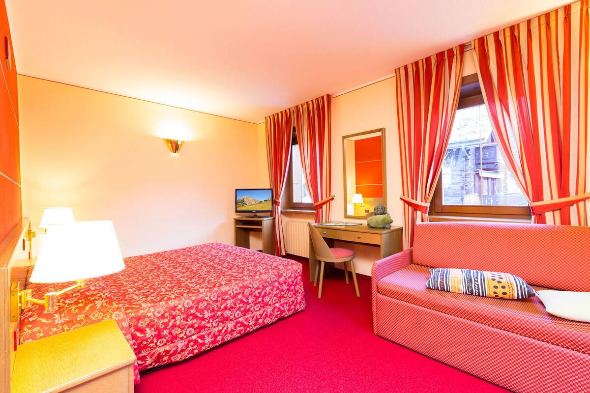 A hotel room with a bed, a desk, a chair, a sofa, and a TV.
