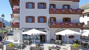 A hotel with a white facade, wooden balconies, and outdoor seating with umbrellas.