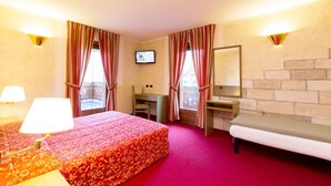 A hotel room with a bed, a desk, a chair, a TV, and a fireplace.
