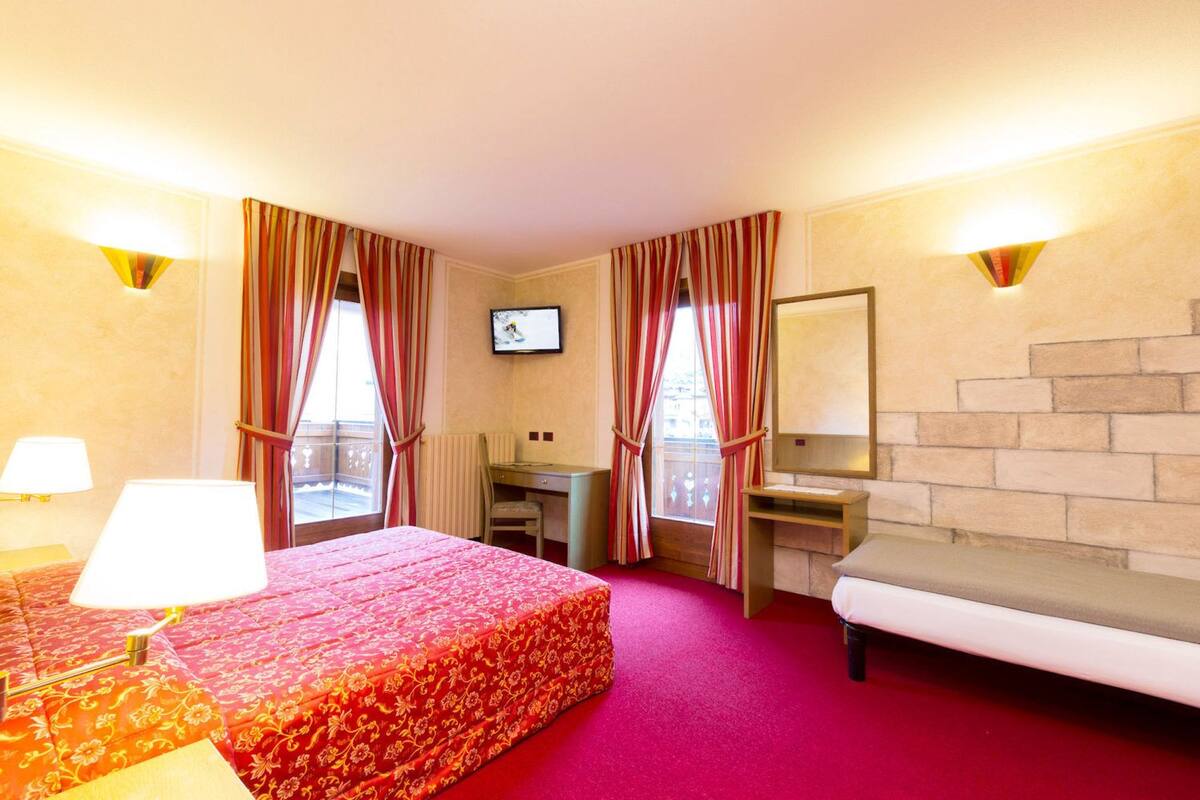 A hotel room with a bed, a desk, a chair, a TV, and a fireplace.