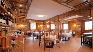 A restaurant with wooden interiors, multiple dining tables, and a bar area with wine bottles.