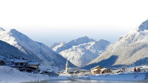 A snow-covered mountain village with traditional wooden houses, a church, and a lake.