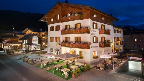 A multi-story hotel with outdoor seating, balconies with flower boxes, and a sign indicating a restaurant.