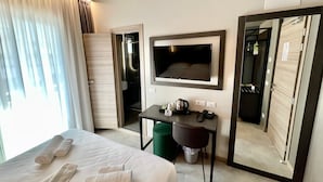 Quarto de hotel com cama, escrivaninha, telefone, televisão e espelho.