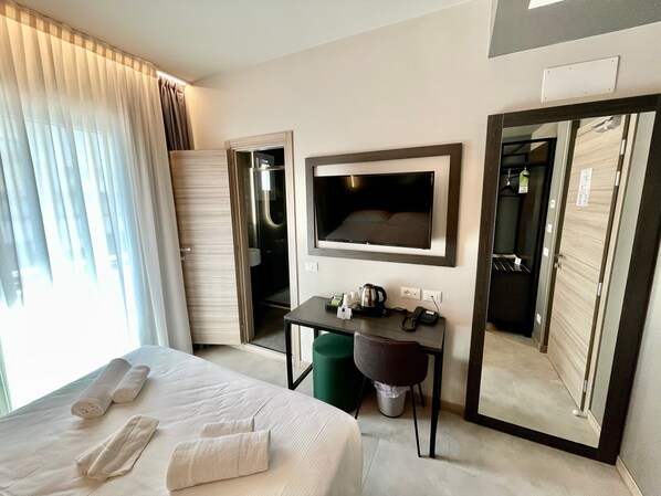 A hotel room with a bed, a desk with a telephone, a television, and a mirror.