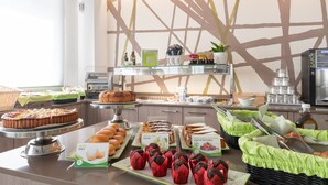 Buffet com diversos alimentos, incluindo doces e bolos, disposto em um balcão com design moderno e uma grande janela ao fundo.