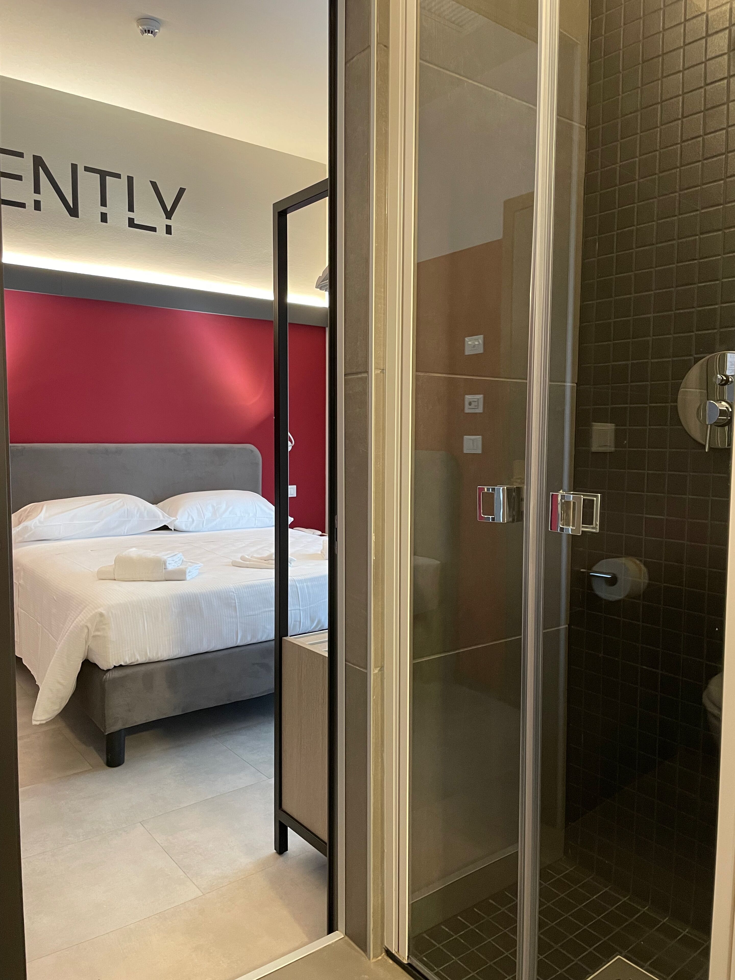 Et hotelværelse med en seng, bruseområde og en rød accentvæg.