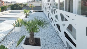 Terraço no telhado com grades brancas, plantas em vasos e céu limpo.
