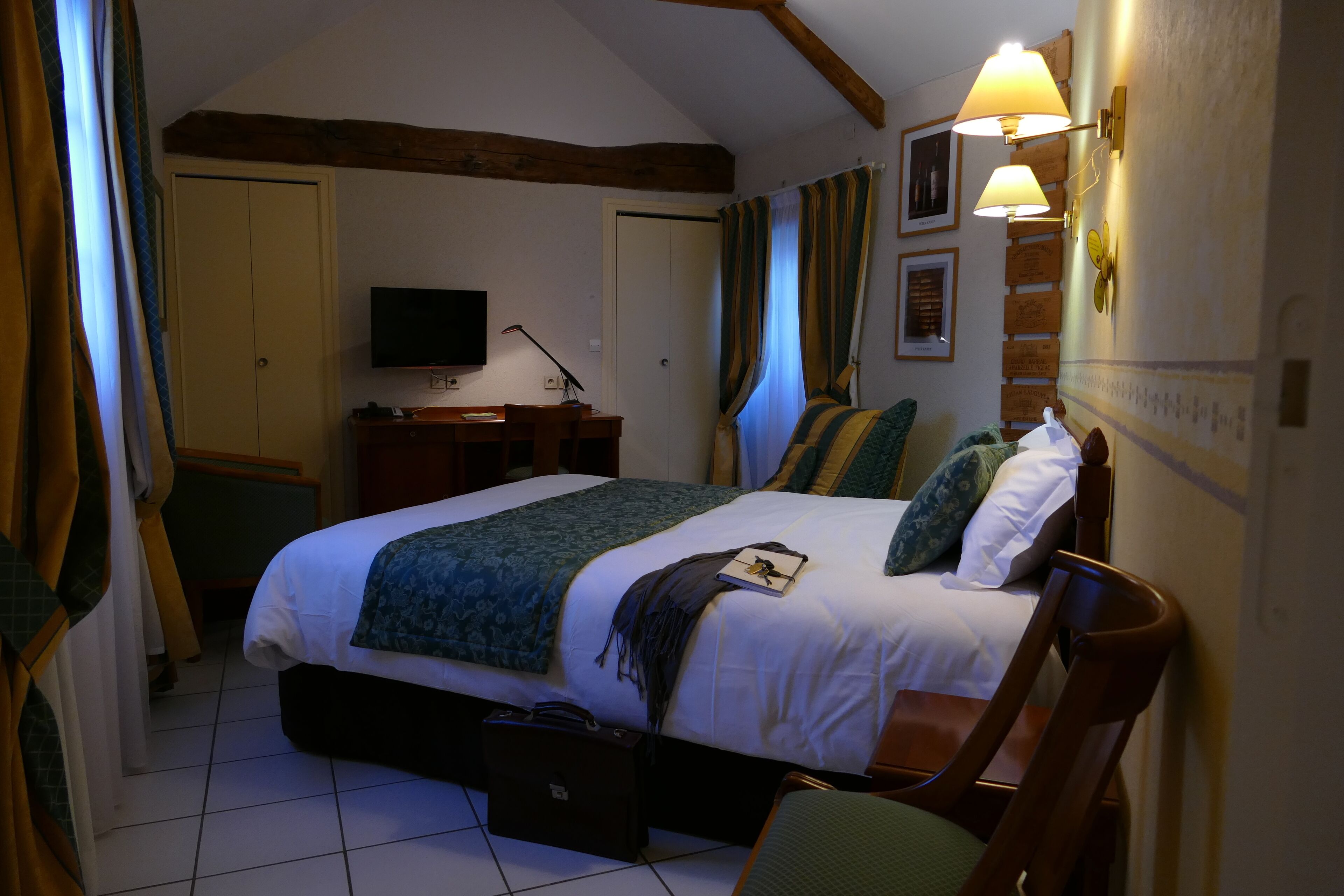 A bedroom with a bed, bedside table, lamp, and a television on the wall.