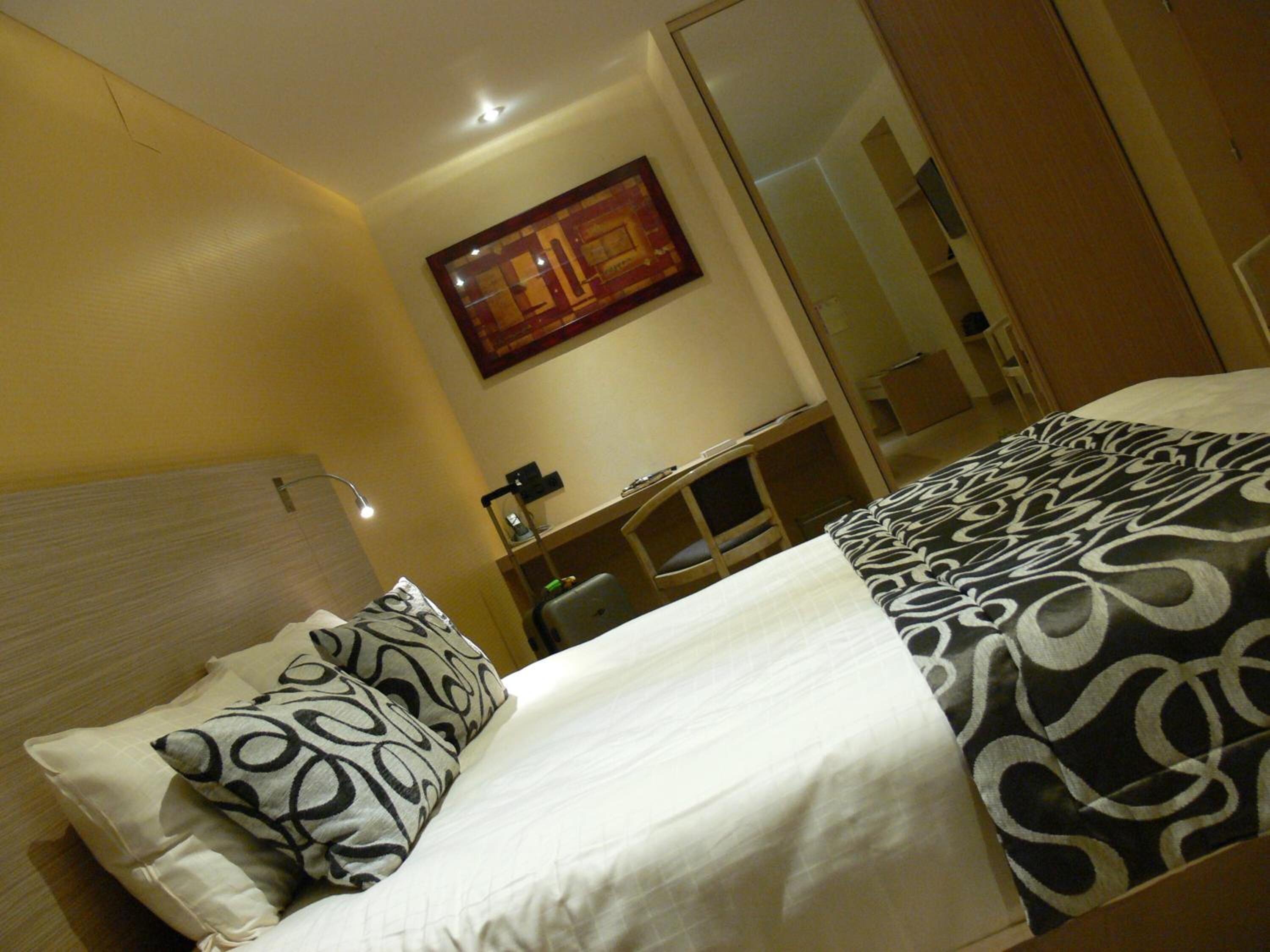 A hotel room with a bed, a desk, and a mirror.
