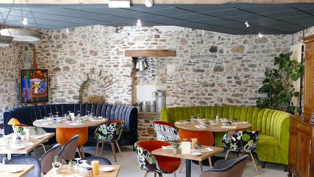 A restaurant with stone walls, wooden tables, and colorful chairs. - Le Champalud (Orée d'Anjou)