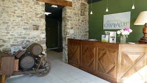 A rustic interior with a stone wall, wooden reception desk, and a vintage bicycle with barrels. - Le Champalud (Orée d'Anjou)