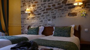 A hotel room with two beds, each with green patterned pillows and a white bedspread. There are two wall-mounted lamps on either side of the bed, and a flower-shaped wall decoration above the right lamp. - Le Champalud (Orée d'Anjou)
