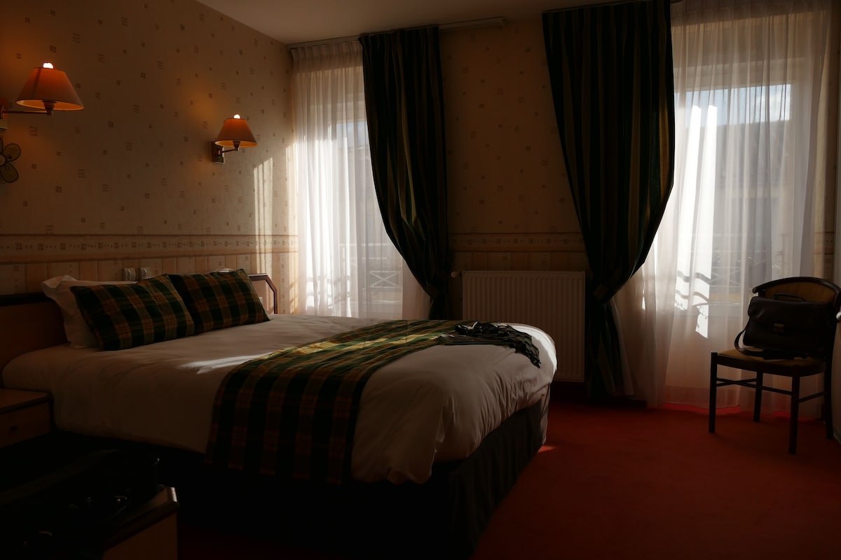 A hotel room with a bed, a chair, a lamp, and a window with curtains.