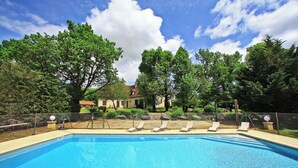 A swimming pool with lounge chairs, surrounded by trees and a fence, with a house in the background. - Hostellerie du Causse (Gramat)