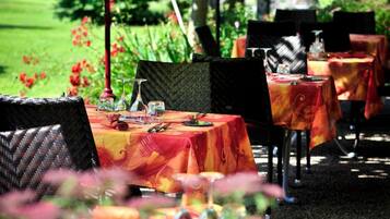 An outdoor dining area with tables covered in tablecloths, surrounded by greenery and trees.