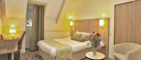 A hotel room with a bed, bedside table, chair, and a small round table with a vase of flowers.