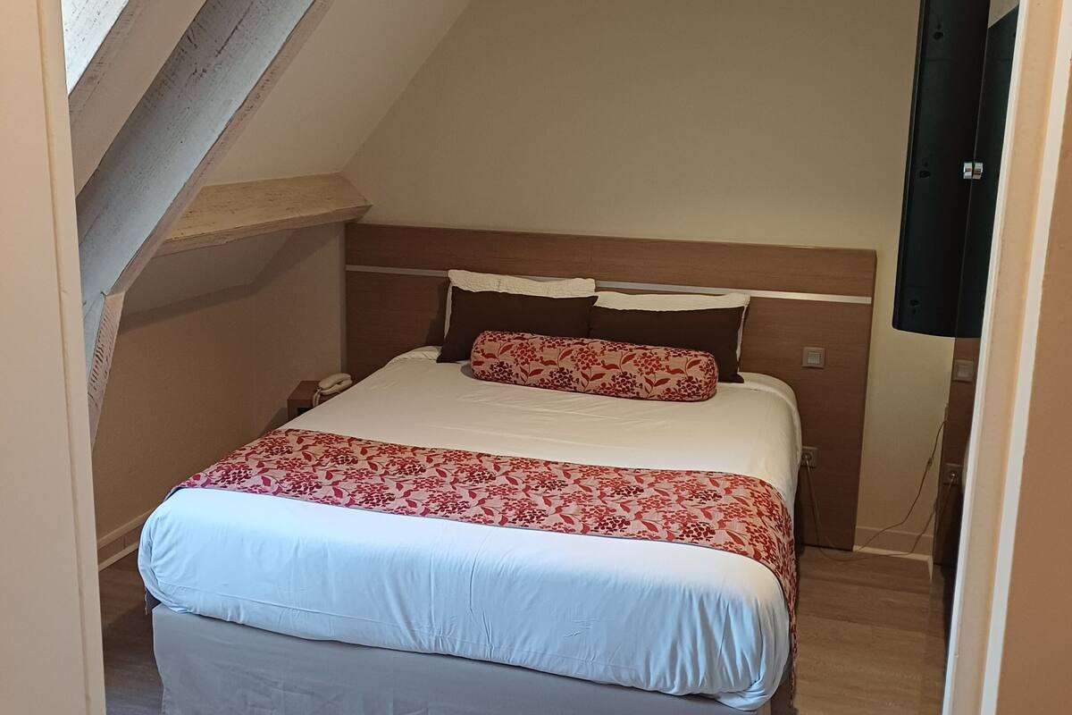 A bedroom with a large bed, a wooden headboard, a sloped ceiling, and a wall-mounted TV.