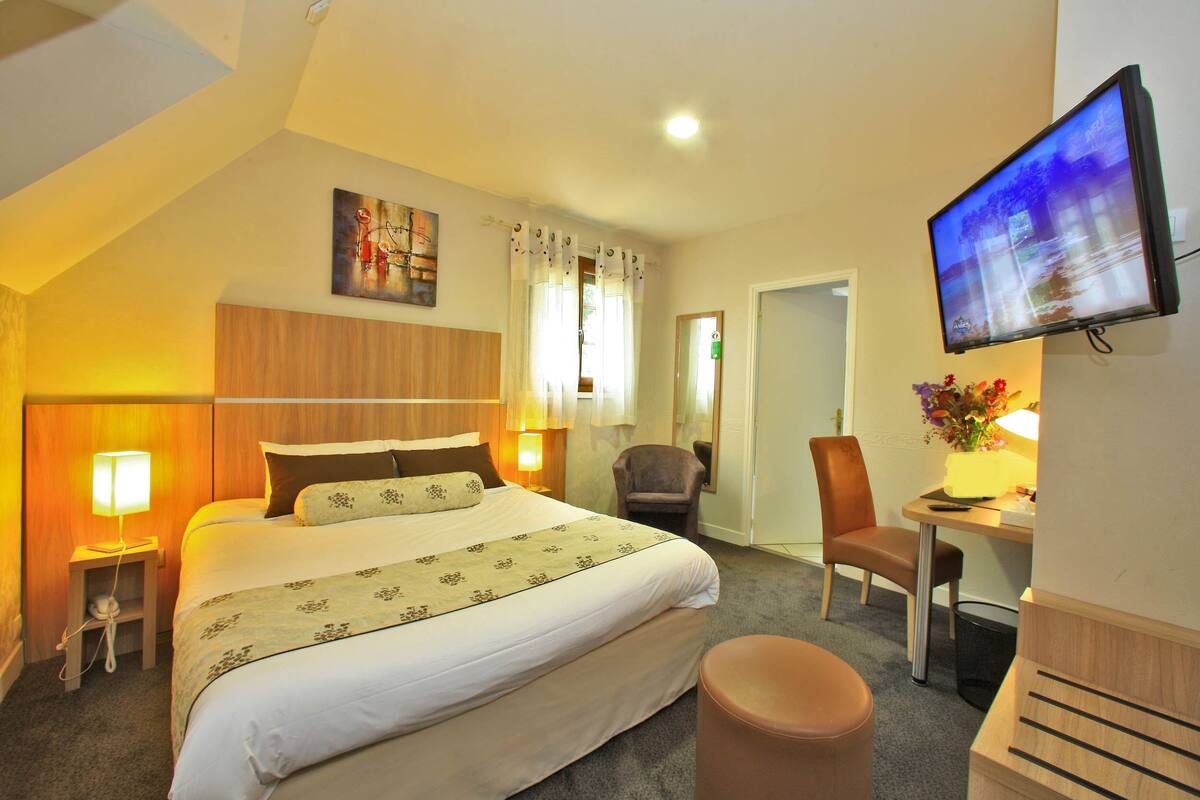 A hotel room with a bed, a desk, a chair, a television, and a painting on the wall.
