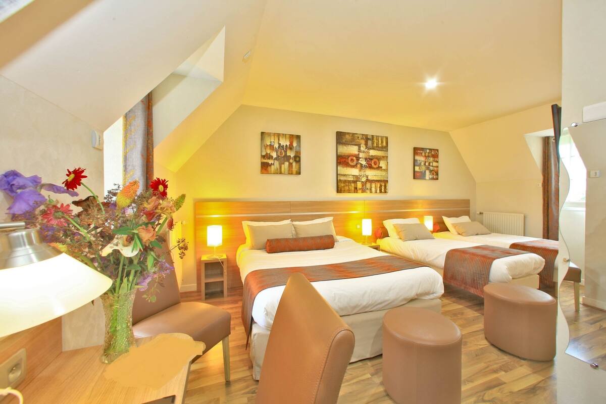 A hotel room with two beds, a desk, a chair, and a vase of flowers.