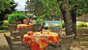An outdoor dining area with wicker chairs and tables, a pool in the background, and a person walking. - Hostellerie du Causse (Gramat)