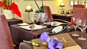 A dining area with a table set for two, featuring a bottle of champagne, wine glasses, and a menu. There is a potted plant and a painting on the wall. - Hostellerie du Causse (Gramat)