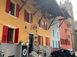 Um hotel com fachada amarela, persianas vermelhas e uma placa indicando que é um hotel.