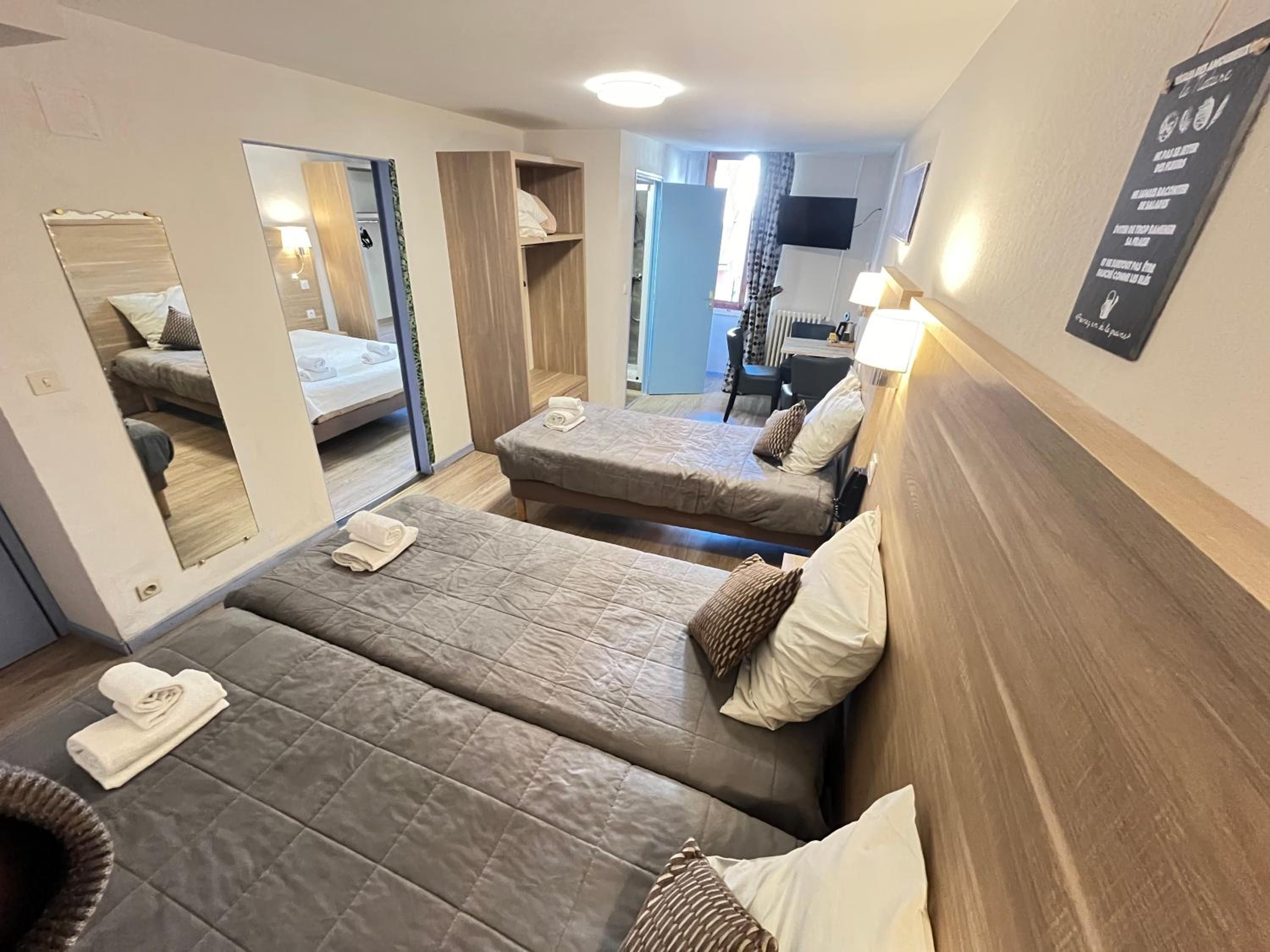Une chambre d’hôtel avec deux lits, un miroir, une télévision et un panneau fixé au mur.