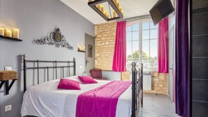 A bedroom with a bed, a chandelier, a stone wall, and a balcony with curtains. - Hôtel restaurant La pêcherie (Courseulles-sur-Mer)
