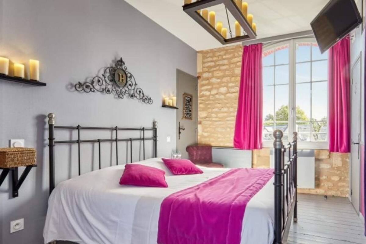 A bedroom with a bed, a chandelier, a stone wall, and a balcony with curtains.