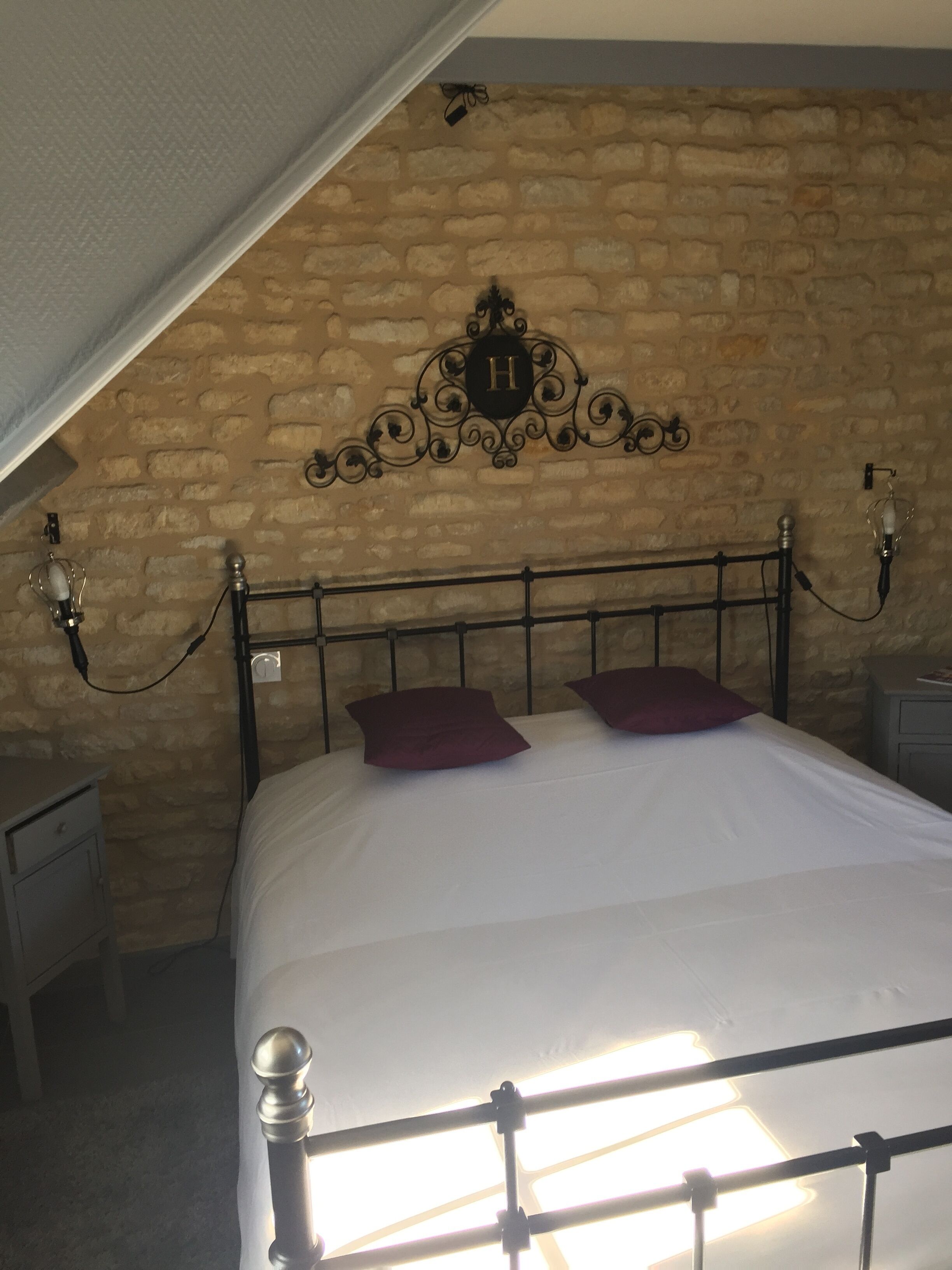 A bedroom with a stone wall, a metal bed frame, and a decorative wall hanging.