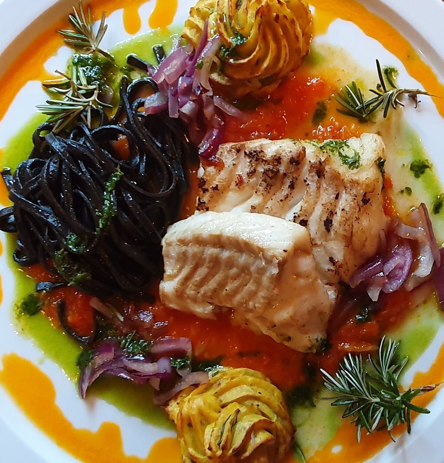 A plate of food with a piece of fish, black pasta, and red onions.