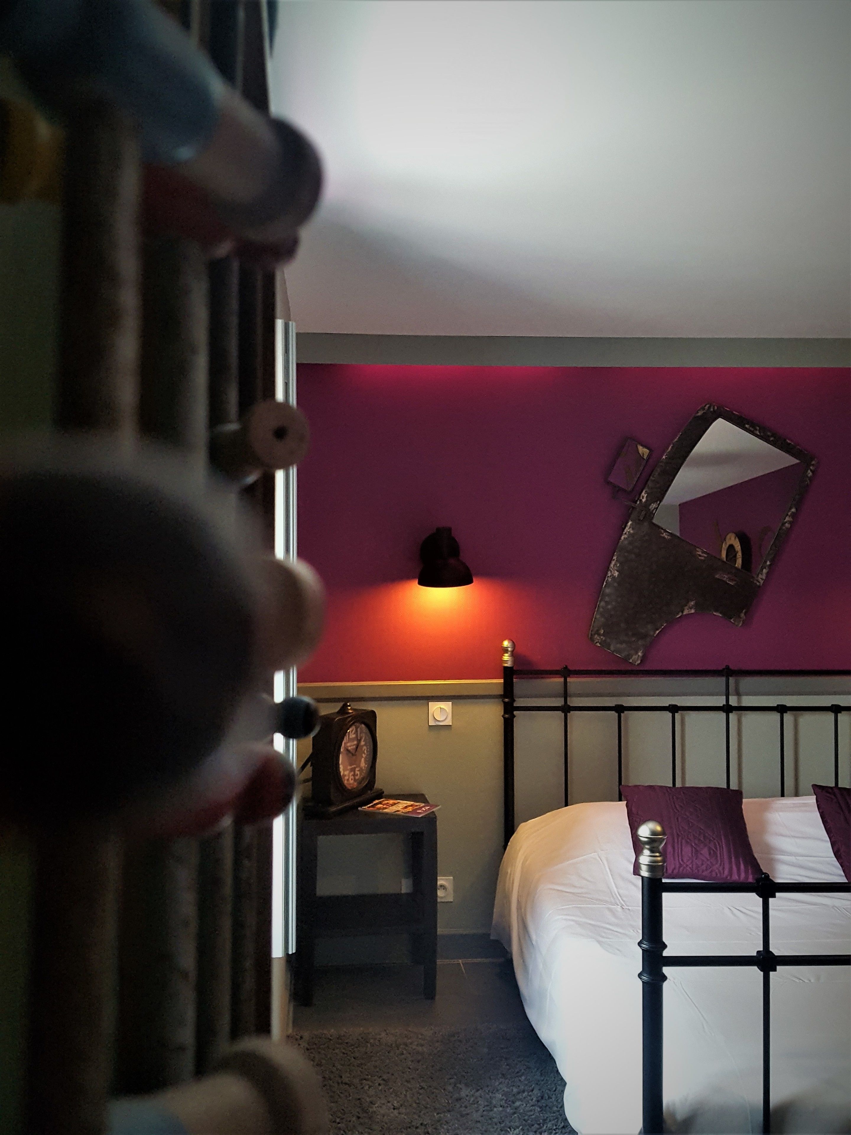 Un dormitorio con cama, mesita de noche, espejo en la pared y un reloj.
