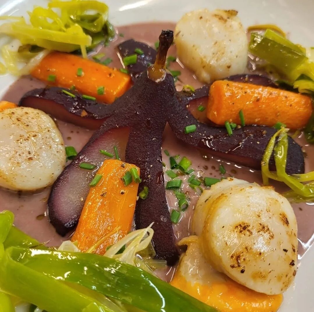 A dish with various vegetables and seafood, including carrots, scallops, and possibly eggplant.