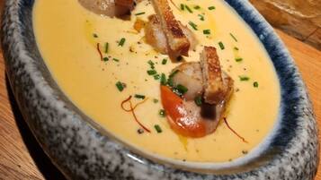 Un tazón de sopa cremosa con pan y cebollines sobre una mesa de madera.