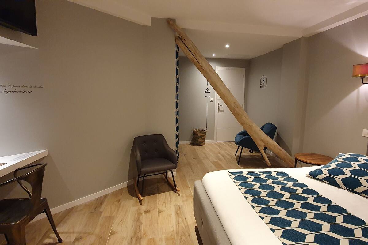 A modern hotel room with a bed, a desk, a chair, and a wooden beam structure.