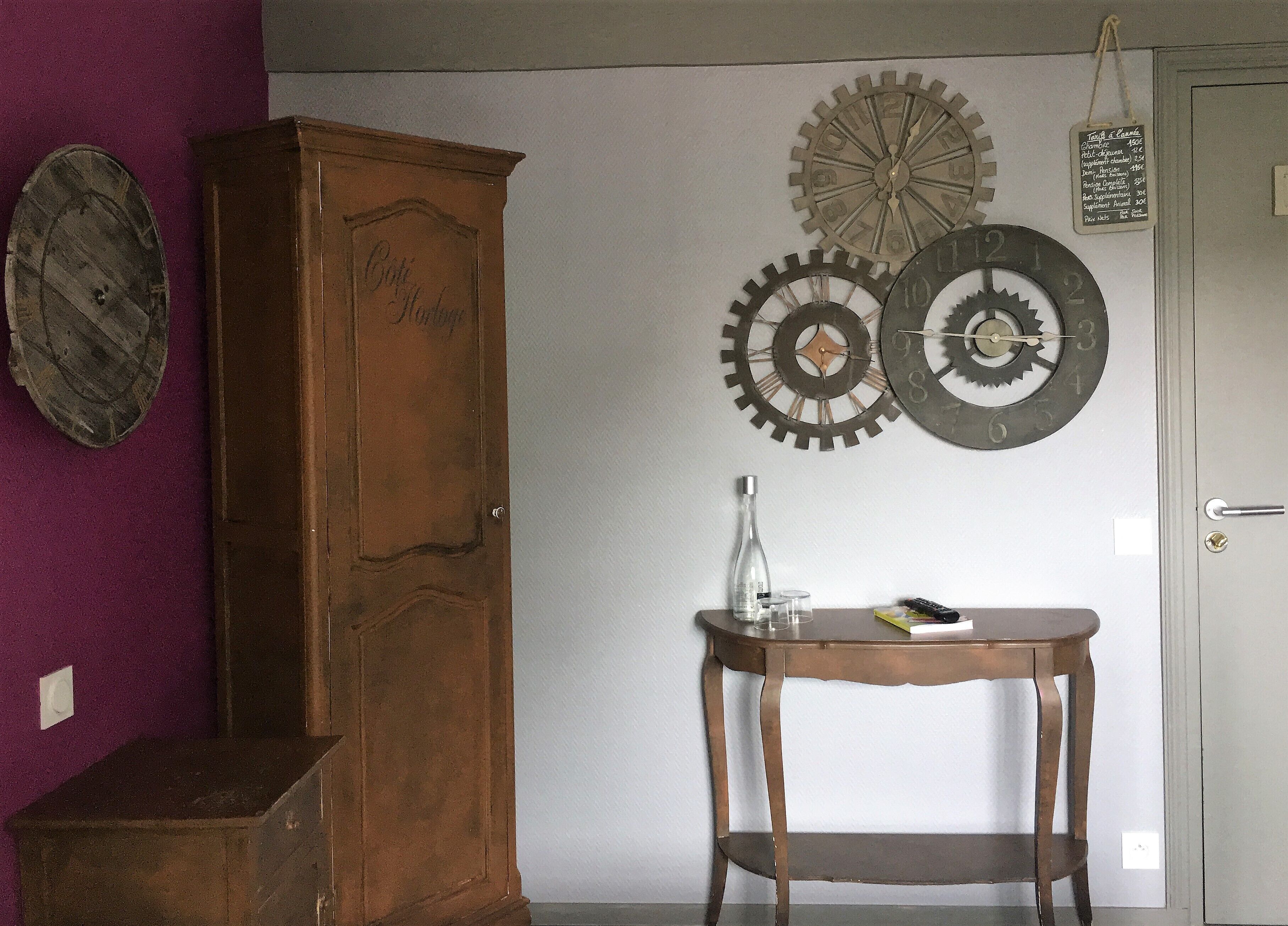 A room with a wooden cabinet, a table with a bottle and glasses, and wall clocks.