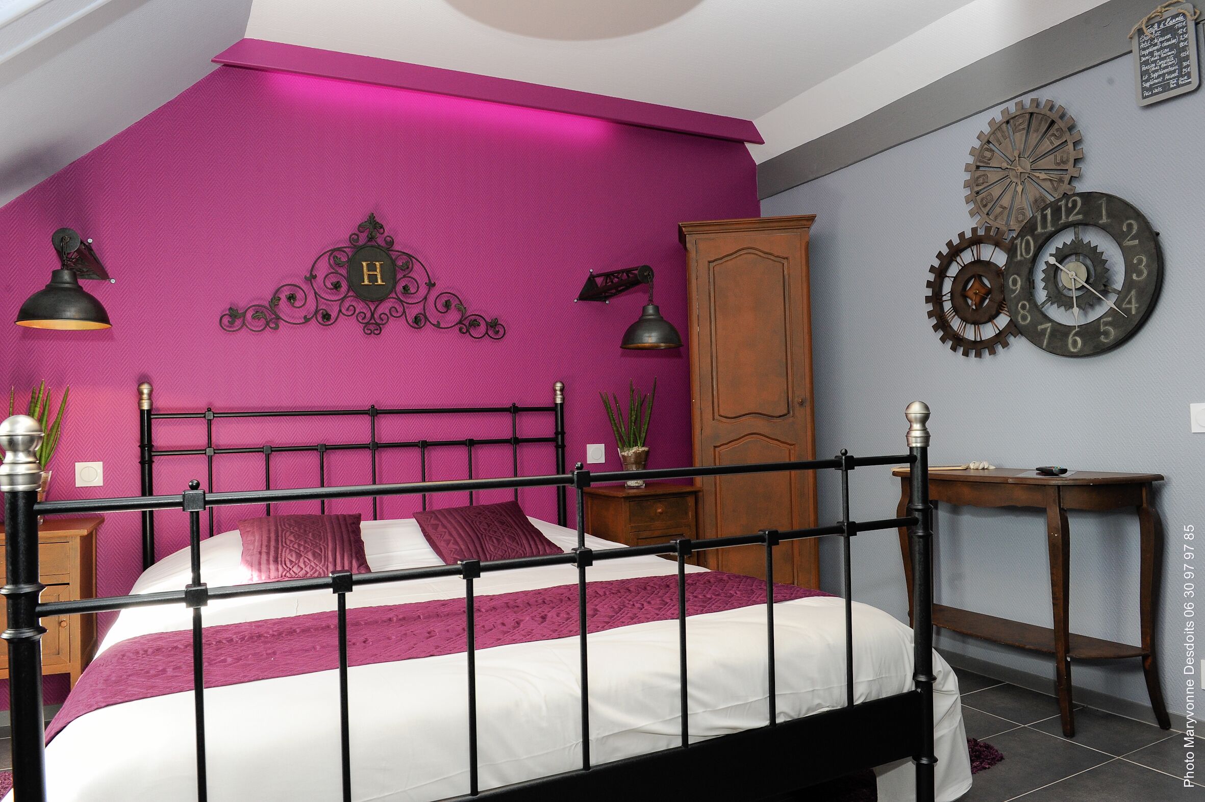 A bedroom with a bed, a wooden wardrobe, a nightstand, a wall clock, and a wall-mounted light fixture.