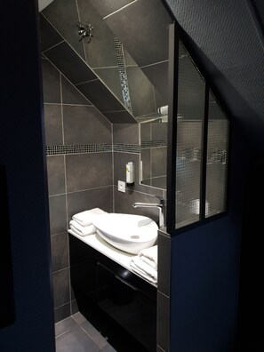 A modern bathroom with a large white sink, dark tiles, and a glass shower enclosure.