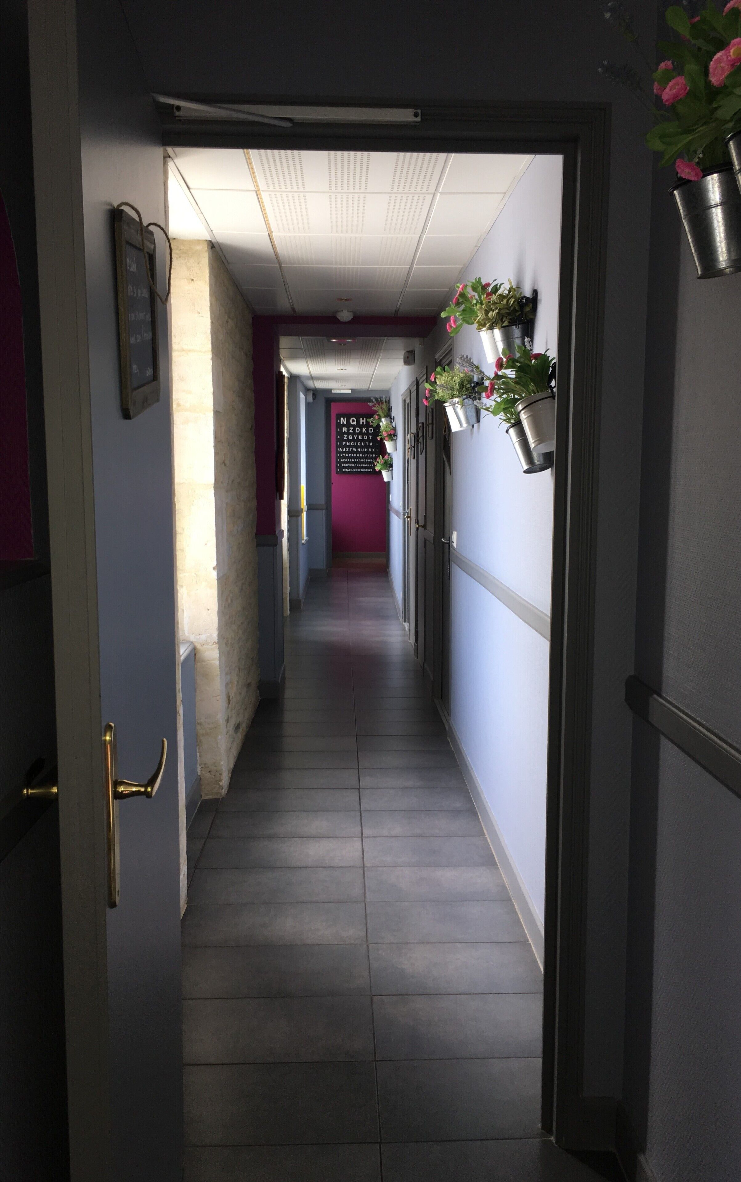 A narrow hallway with a tiled floor, a door on the left, and a wall-mounted sign on the right.