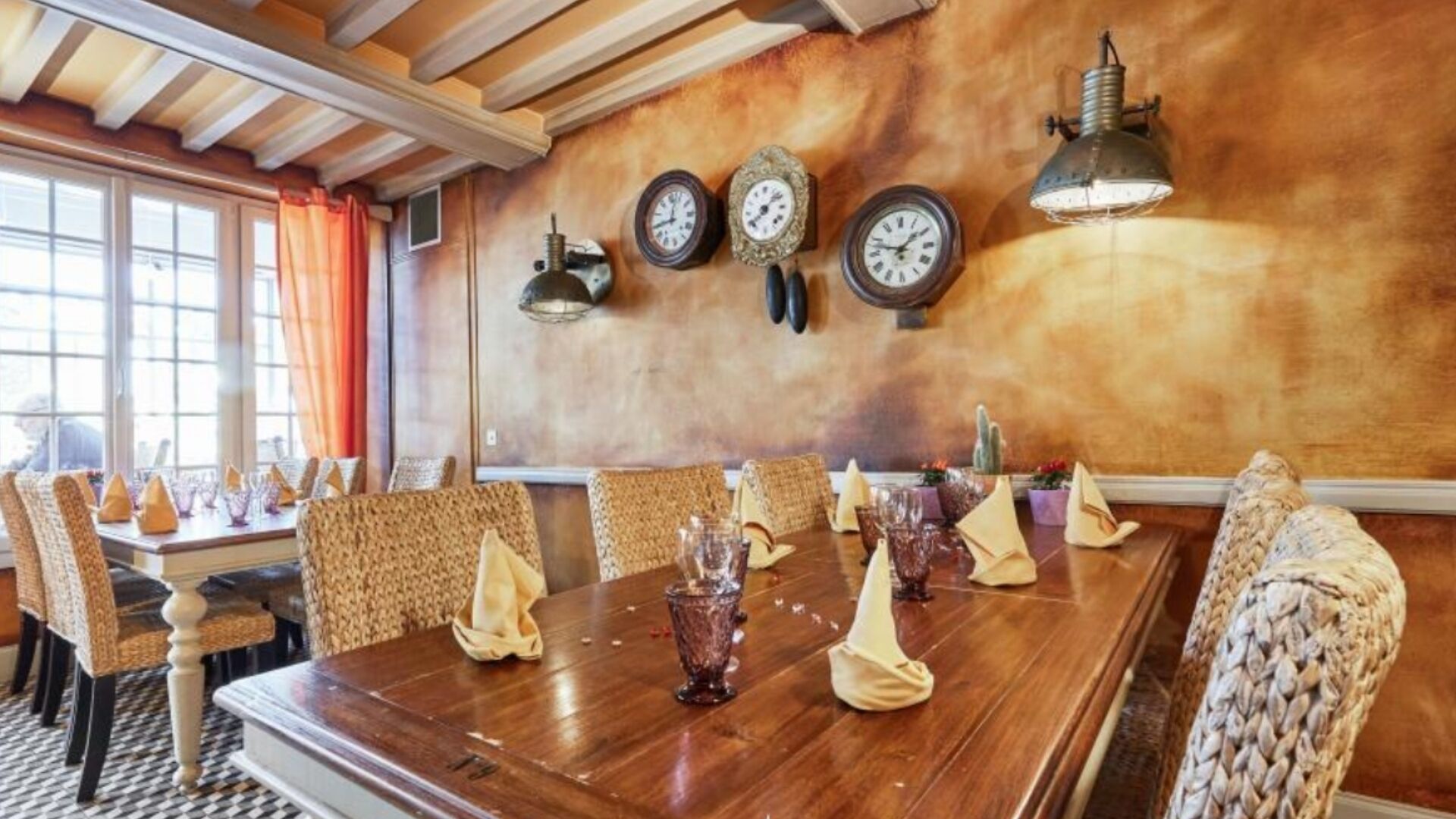 A dining area with a wooden table set for a meal, surrounded by wicker chairs.
