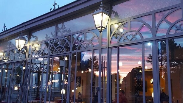 A covered outdoor seating area with glass walls, metal railings, and decorative lighting. - Hôtel restaurant La pêcherie (Courseulles-sur-Mer)