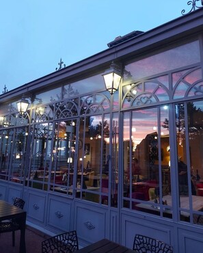 A covered outdoor seating area with glass walls, metal railings, and decorative lighting. - Hôtel restaurant La pêcherie (Courseulles-sur-Mer)