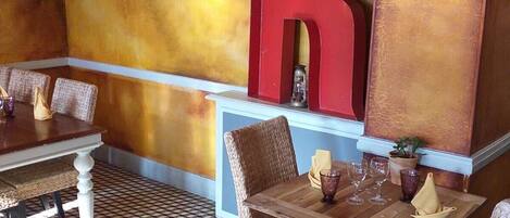 A restaurant with a checkered floor, wicker chairs, wooden tables, a large red letter 'R' on the wall, and pendant lights.