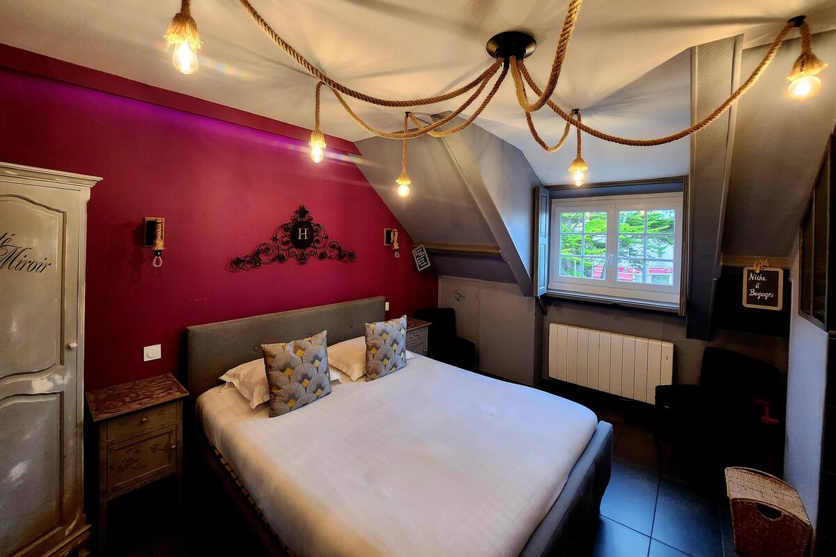 A bedroom with a bed, a nightstand, a dresser, a window with a view, and a ceiling with rope lights.
