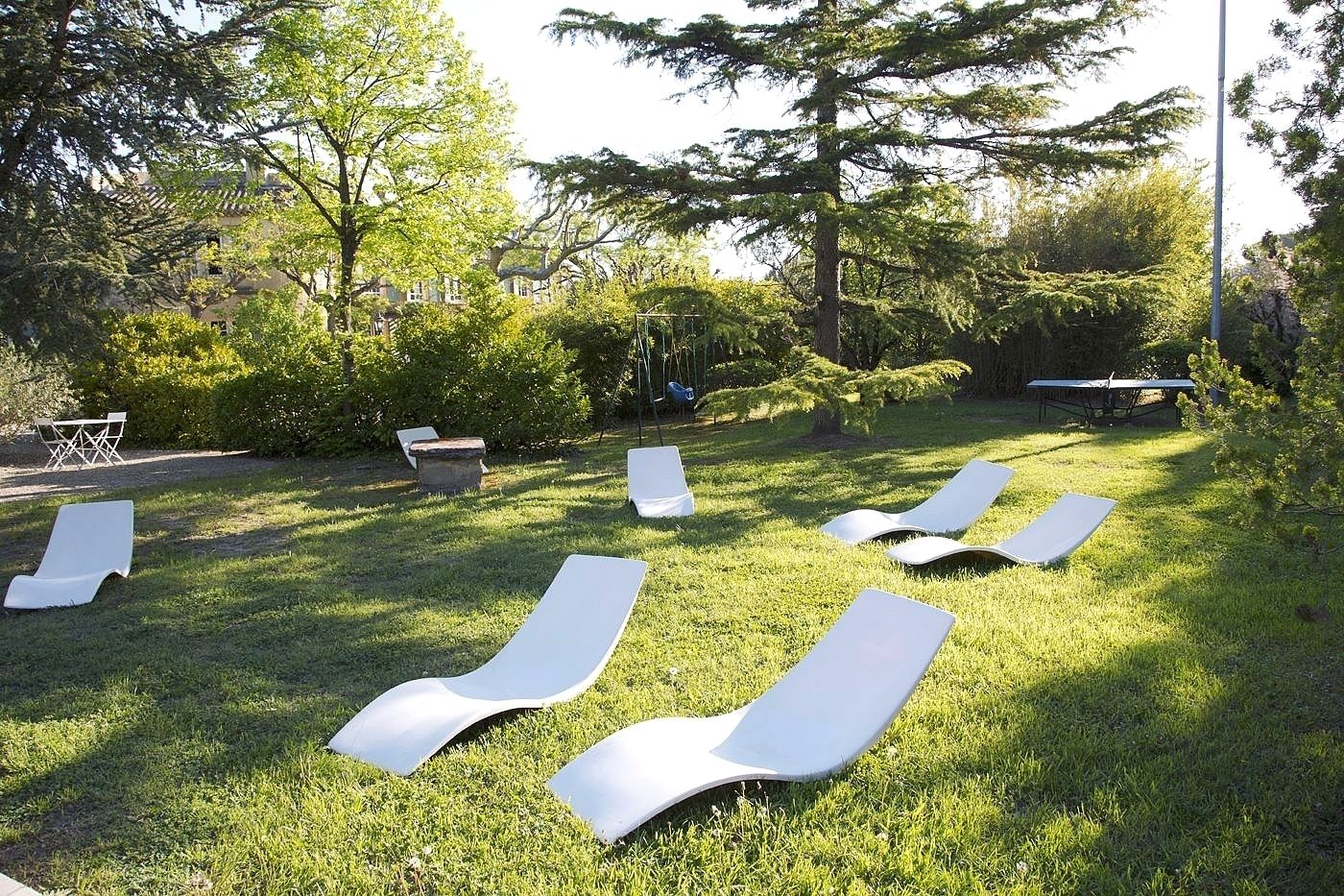 A grassy outdoor area with several white lounge chairs and a small table.
